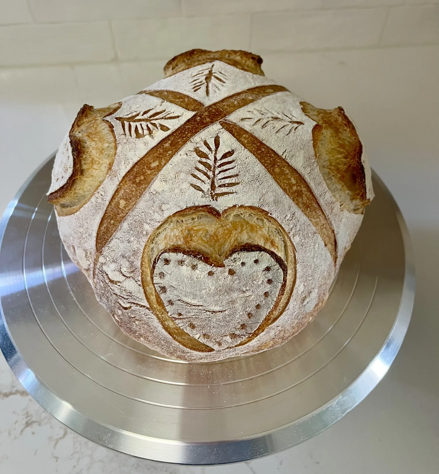 A round sourdough loaf with a heart and leaf pattern scored into its golden crust